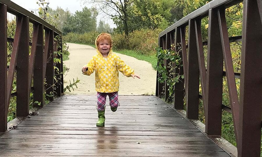 A young child in a yellow jacket runs across a bridge.