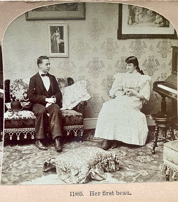 A young couple sit on opposite chairs in a living room in this old photograph.