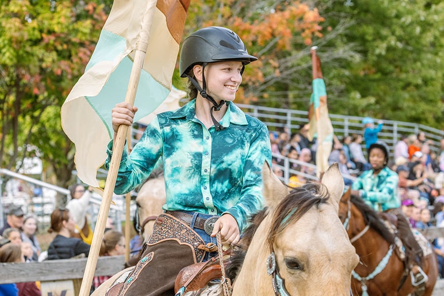 A woman holding a flag as she rides a horse