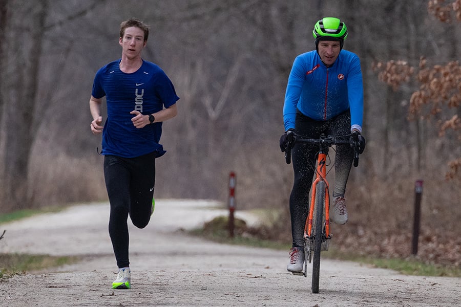 a man jogging next to a man biking on a trail a man jogging next to a man biking on a trail