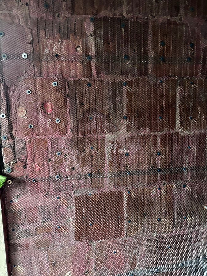 A mesh lath resembles a metal screen resting against exposed bricks.