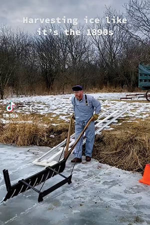 man on frozen lake cutting ice with a saw