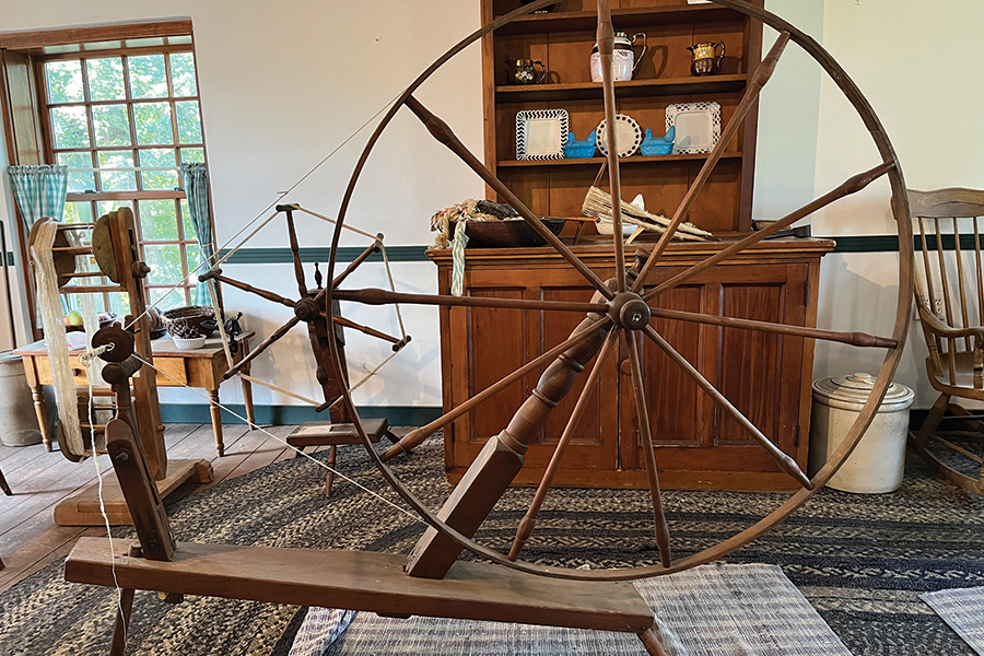 A wooden wheel contraption is used to turn fibers into yarn.
