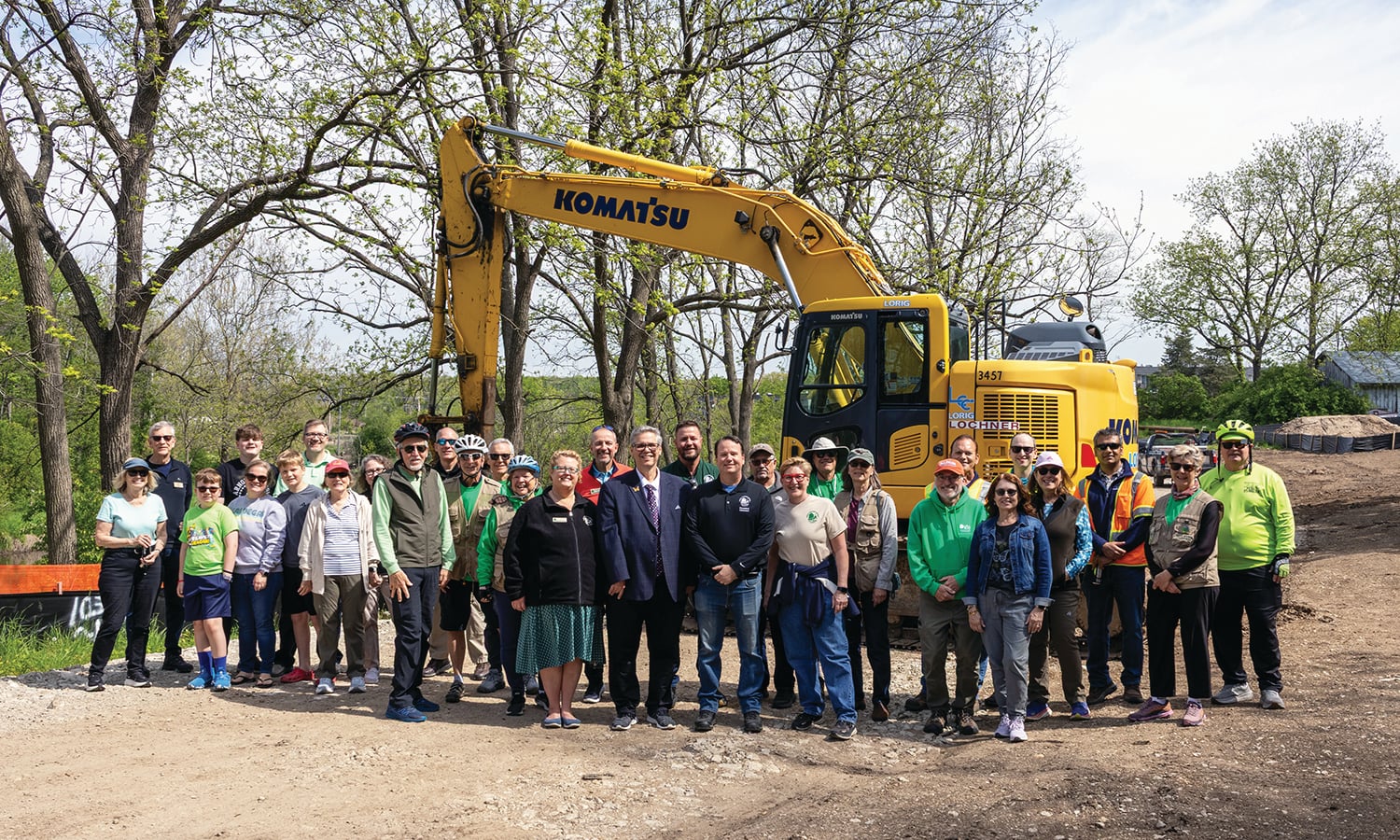 A group of people stand in front of a construction machine in a forest preserve.