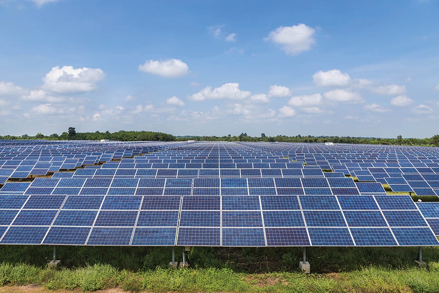 A field of solar panels absorb sunlight under a slightly cloudy sky.