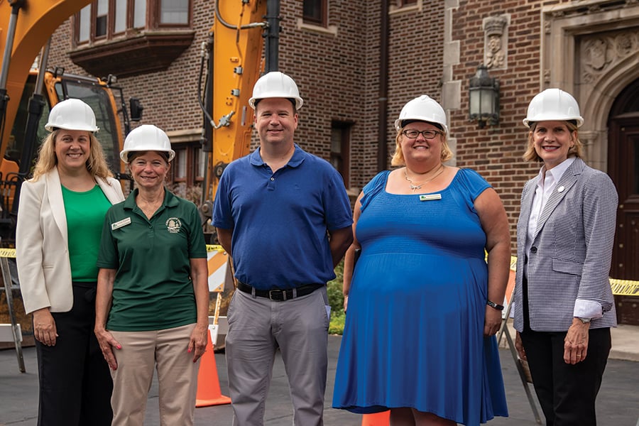 five people in hardhats in front a piece of construction equipment in front of Mayslake Hall
