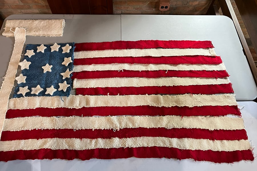 Handmade American flag in progress with red and white wool stripes, a blue canton and felted white stars laid out on a table before final assembly.