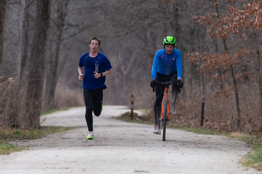 A cyclist passes a jogger on the left, using proper trail etiquette.