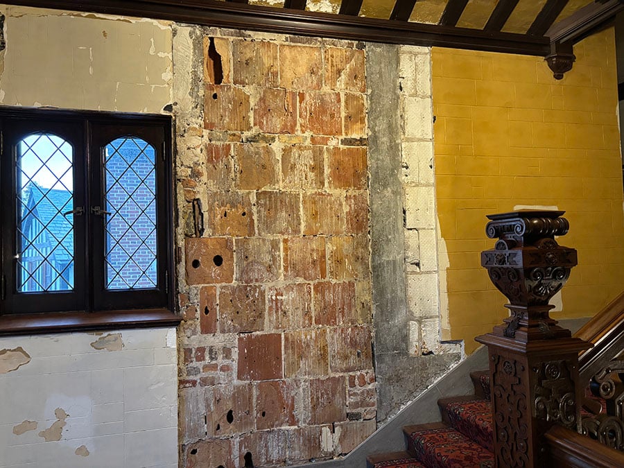 An exposed brick wall in a stairway has holes and gaps in it.